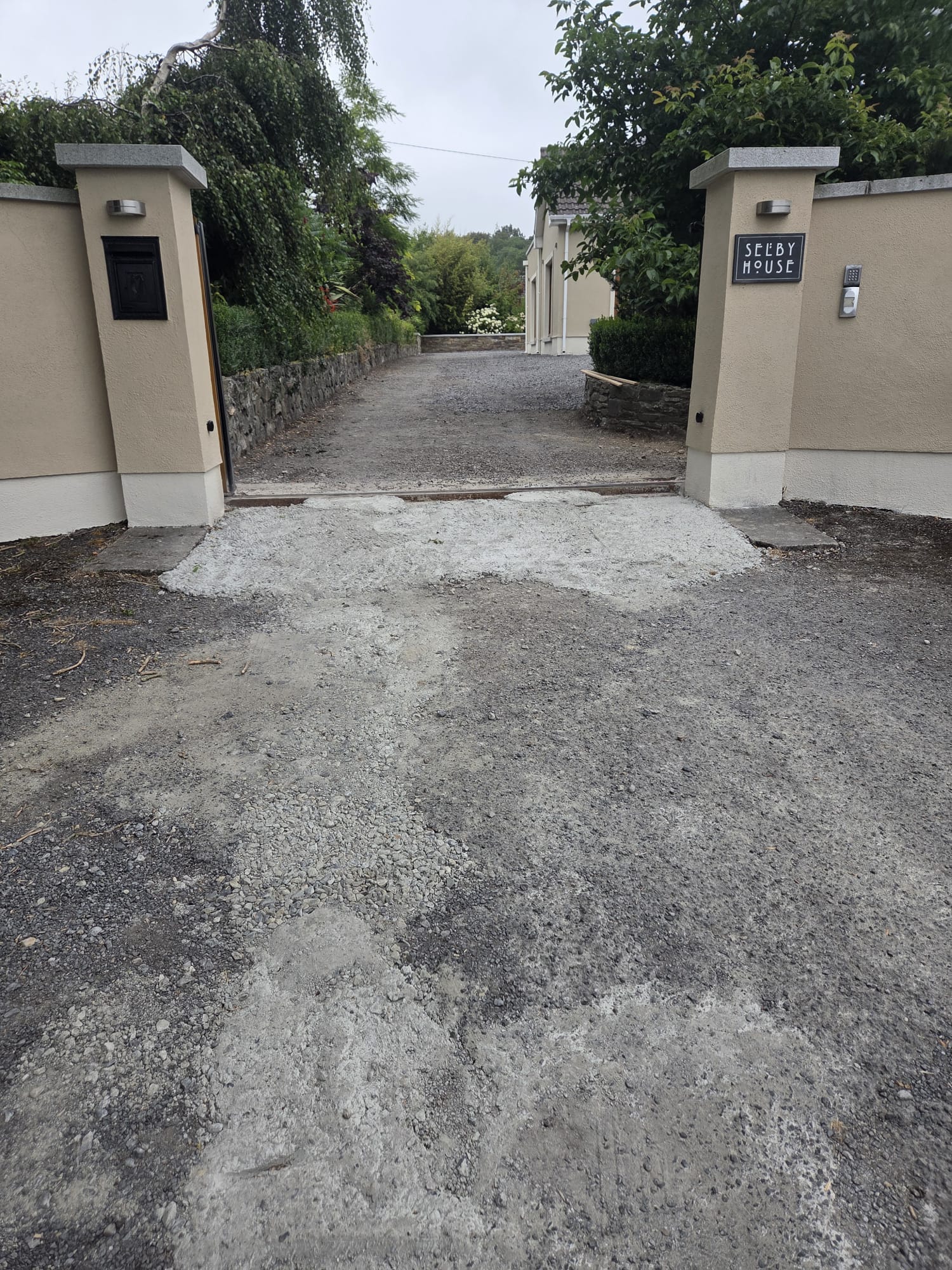 A gated country entrance before the rebuild, its gravel and hardcore surface broken up, patchy and settled unevenly