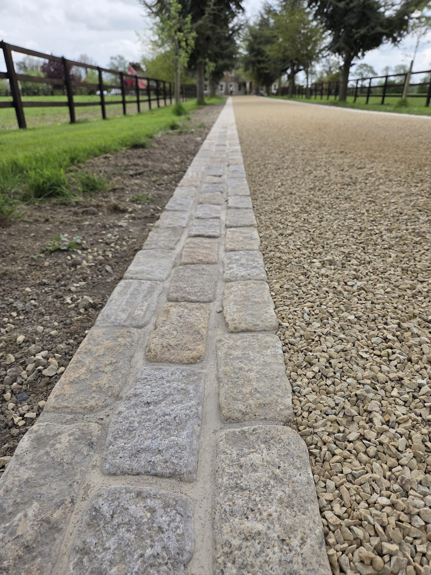 Granite cobble sett border between fence and gravel driveway