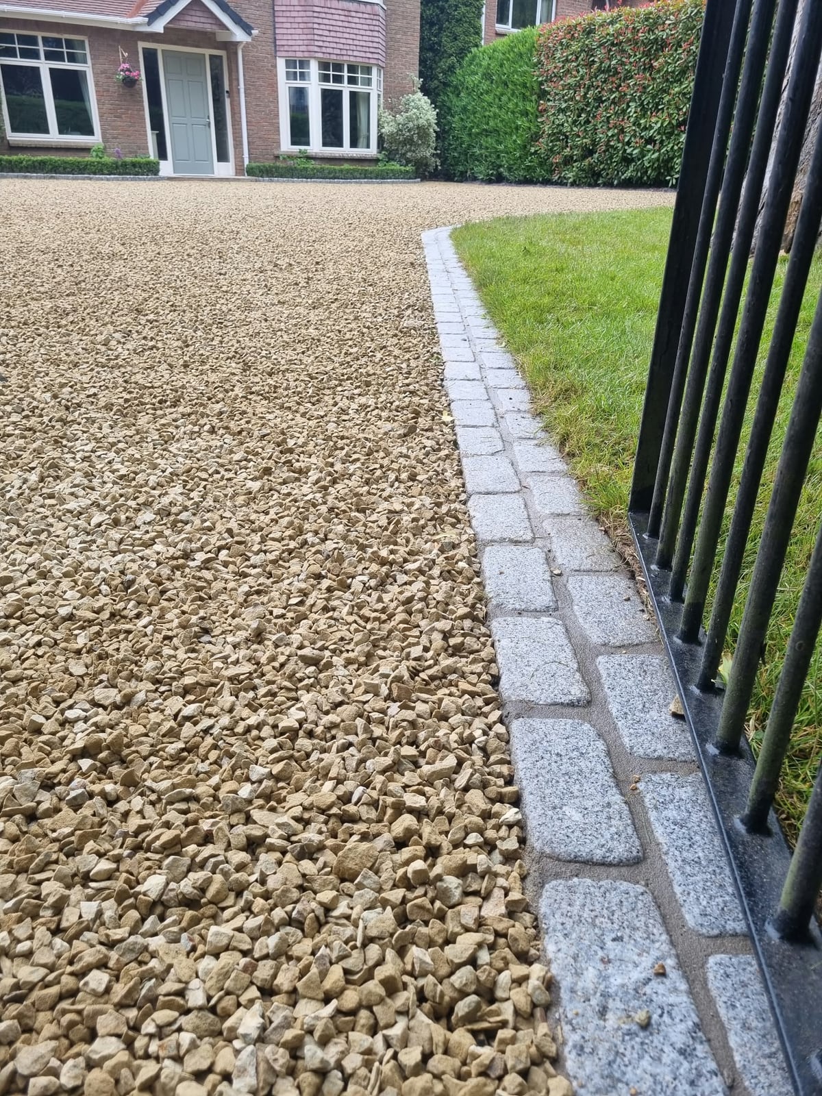 Granite setts between the gravel driveway and the lawn, beside the gate railings