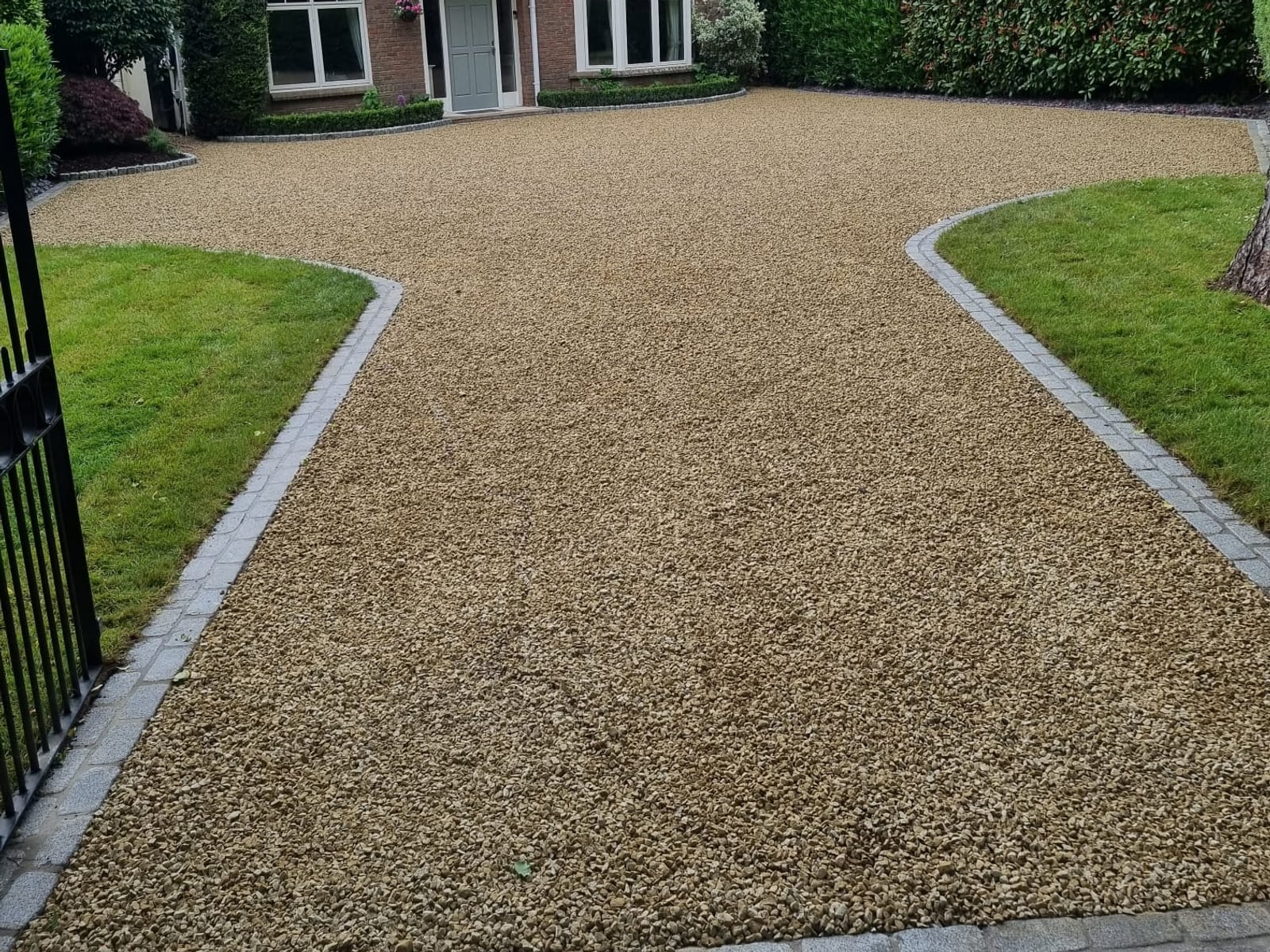 Gravel driveway between two lawns with granite sett edging and a granite cobble apron at the gate, laid by Delaney Tarmac