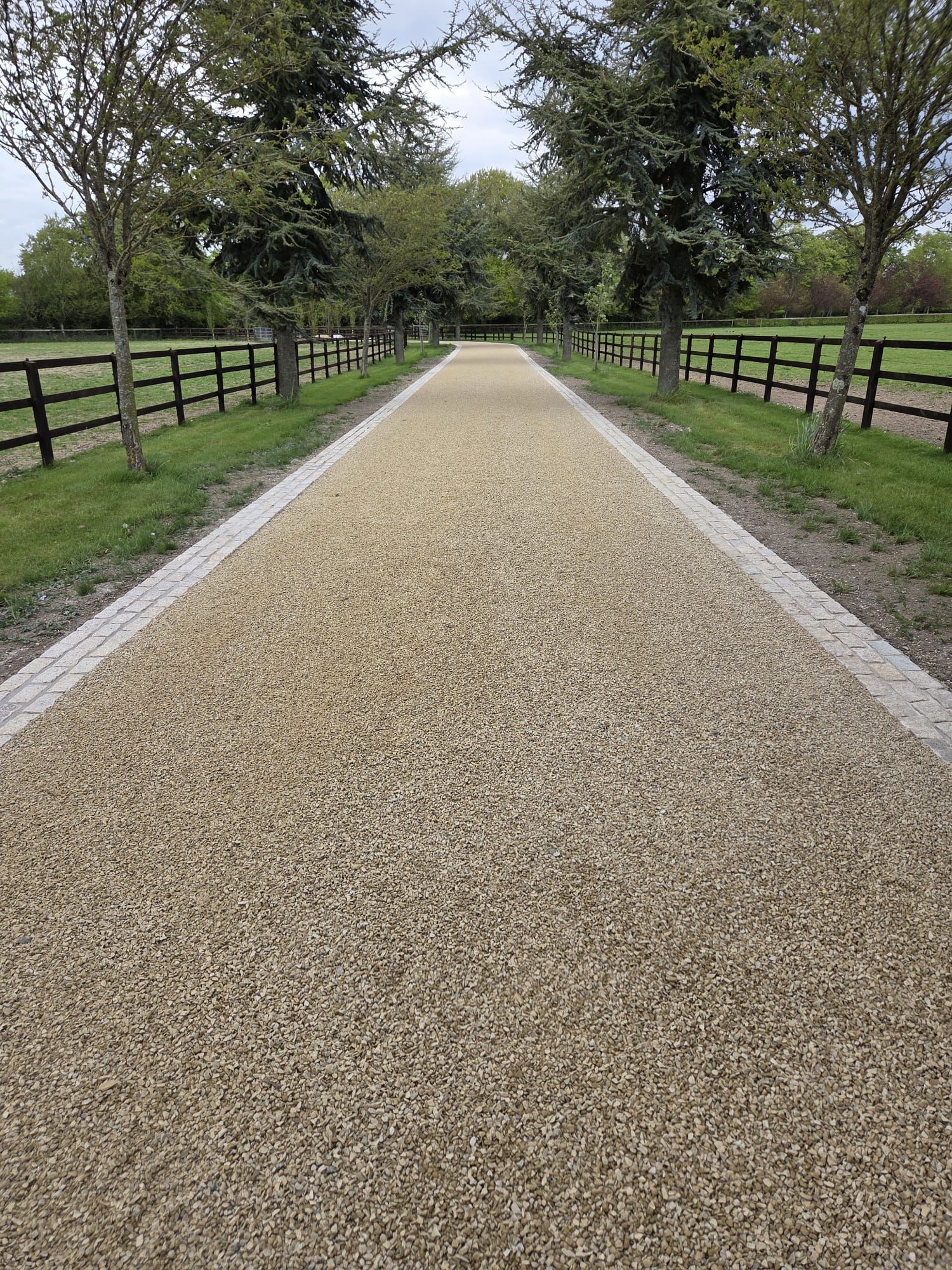Golden gravel driveway between black post-and-rail fencing