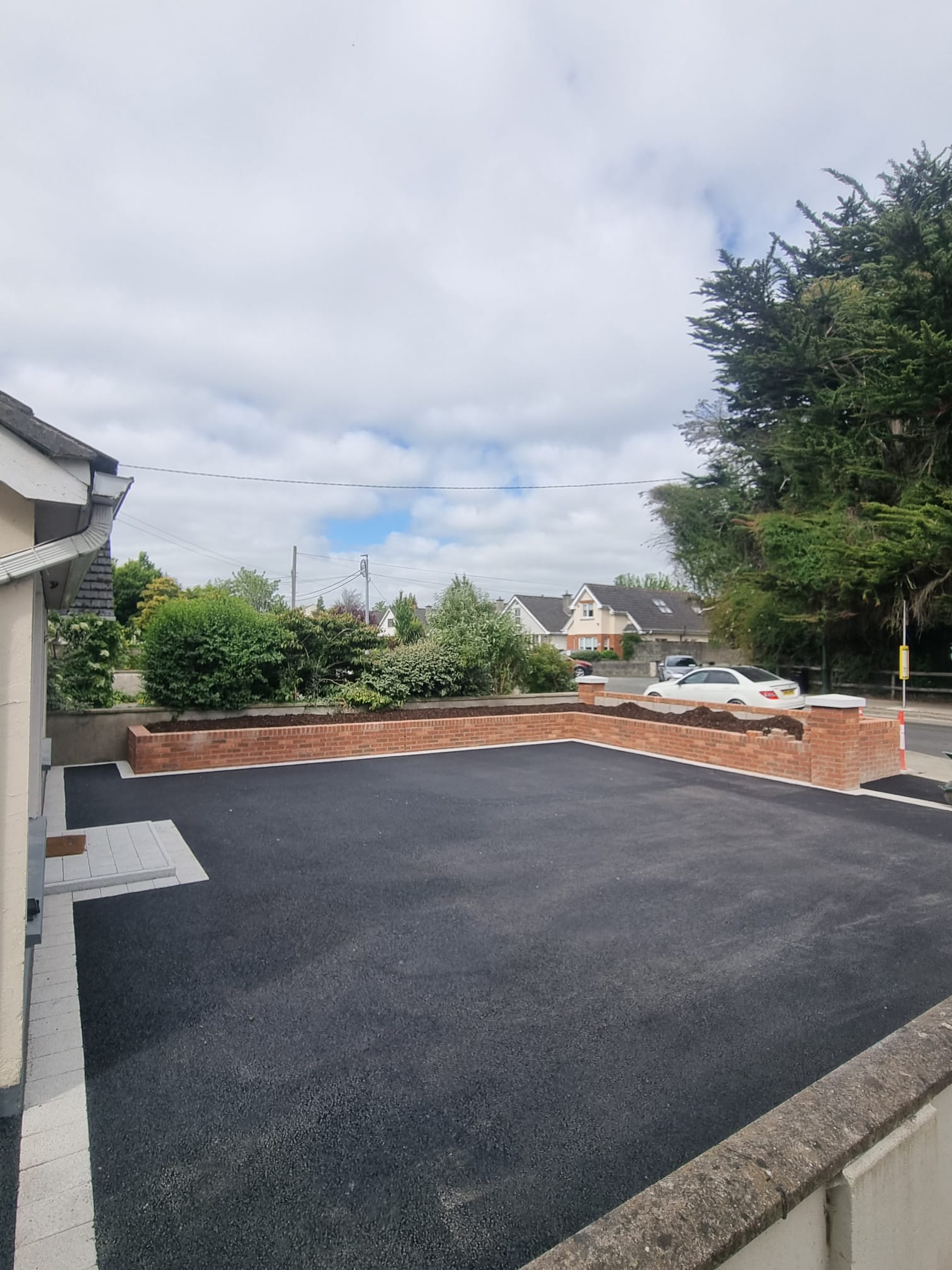 New tarmac driveway with a red-brick boundary wall and raised planter