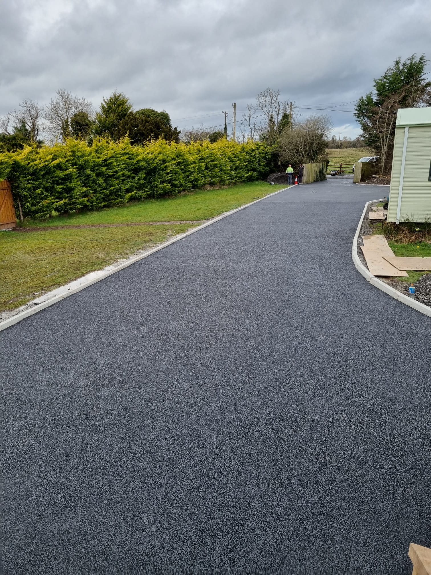 A long new tarmac access road with concrete kerbs along both edges