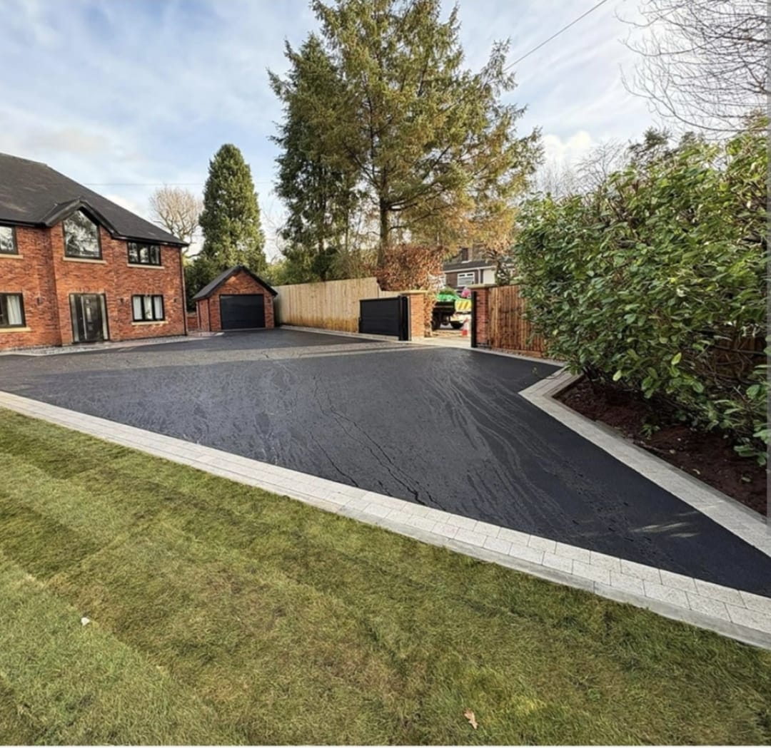Large tarmac driveway with a silver granite cobble border at a red-brick two-storey home