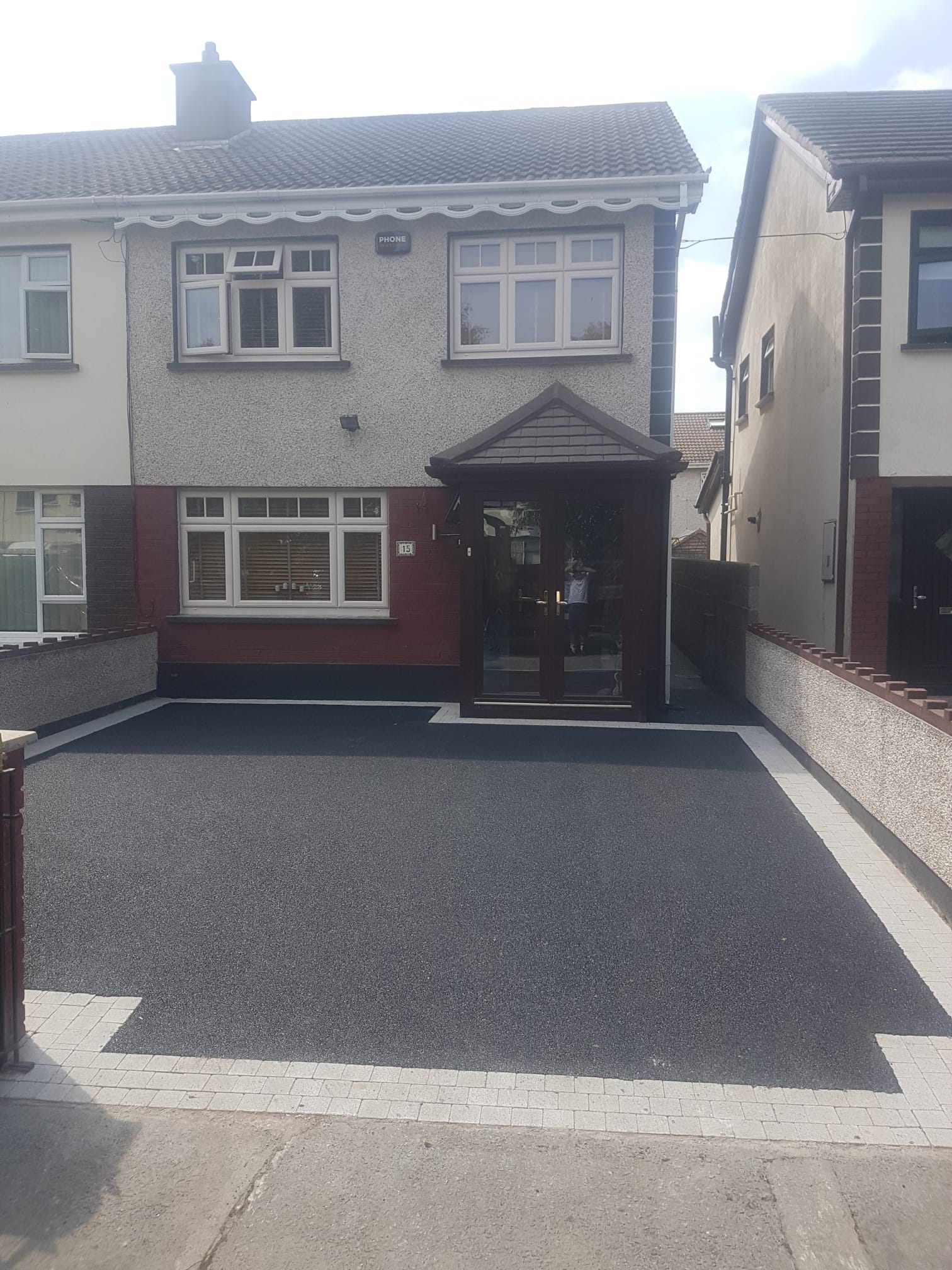 Tarmac driveway at a grey pebbledash semi-detached home with red brick lower and porch entry