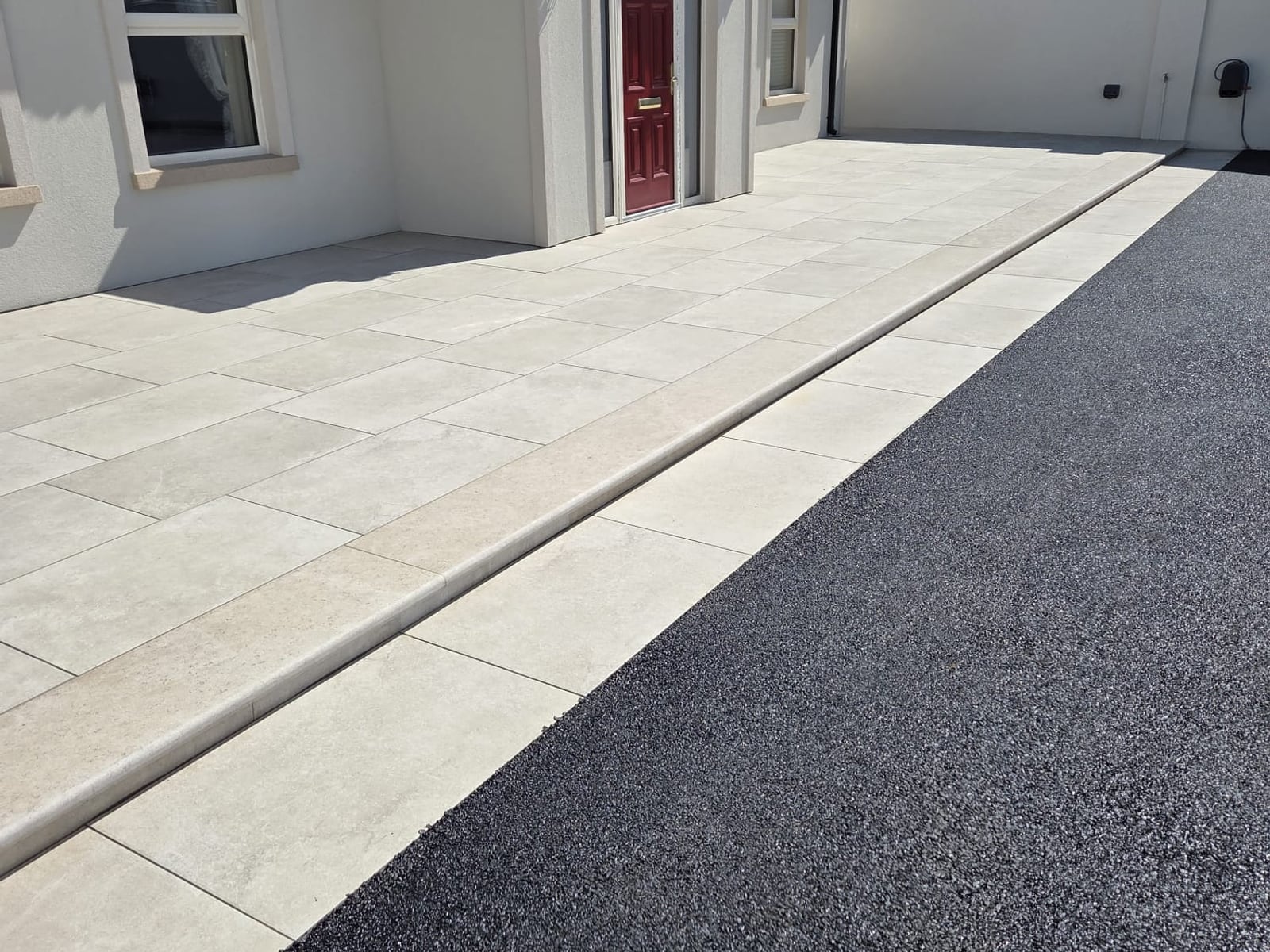 Tarmac driveway meeting a pale paved apron and step at the red front door of a new bungalow, laid by Delaney Tarmac