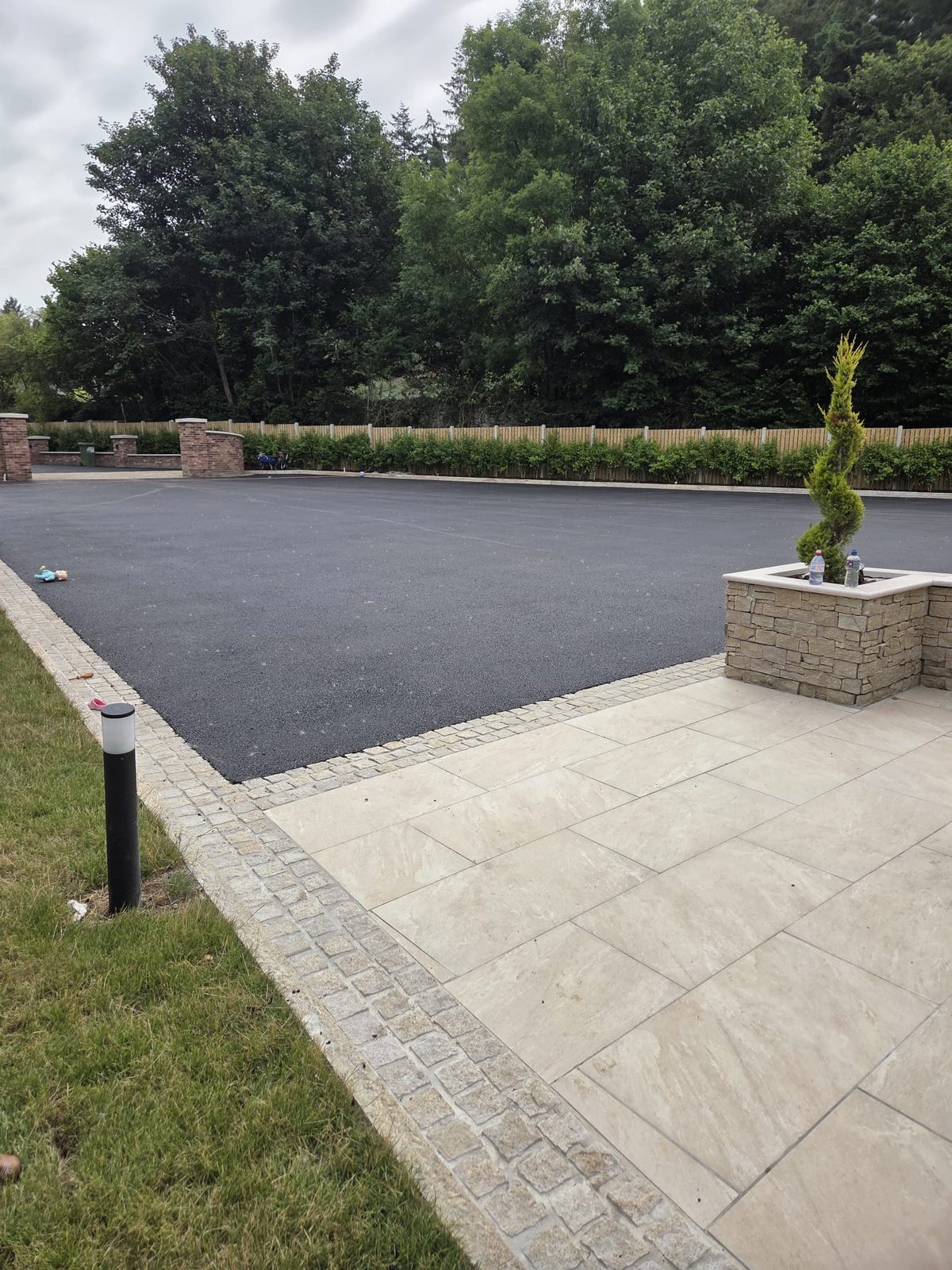 Tarmac forecourt meeting a cream paved patio with a stone-clad planter and cobble border at a country home