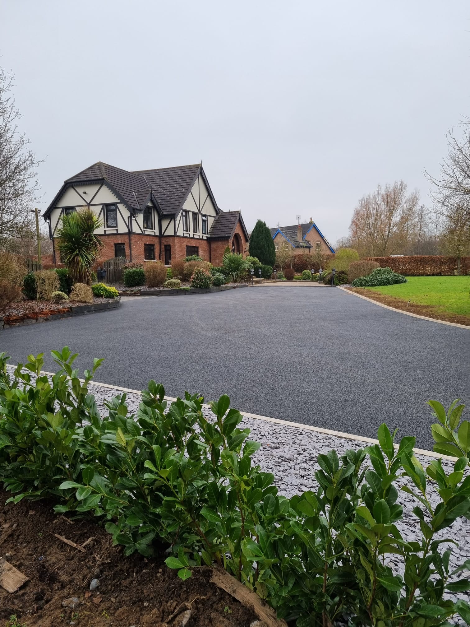 Tarmac driveway sweeping toward a brick Tudor country house with planted island and granite cobble bands