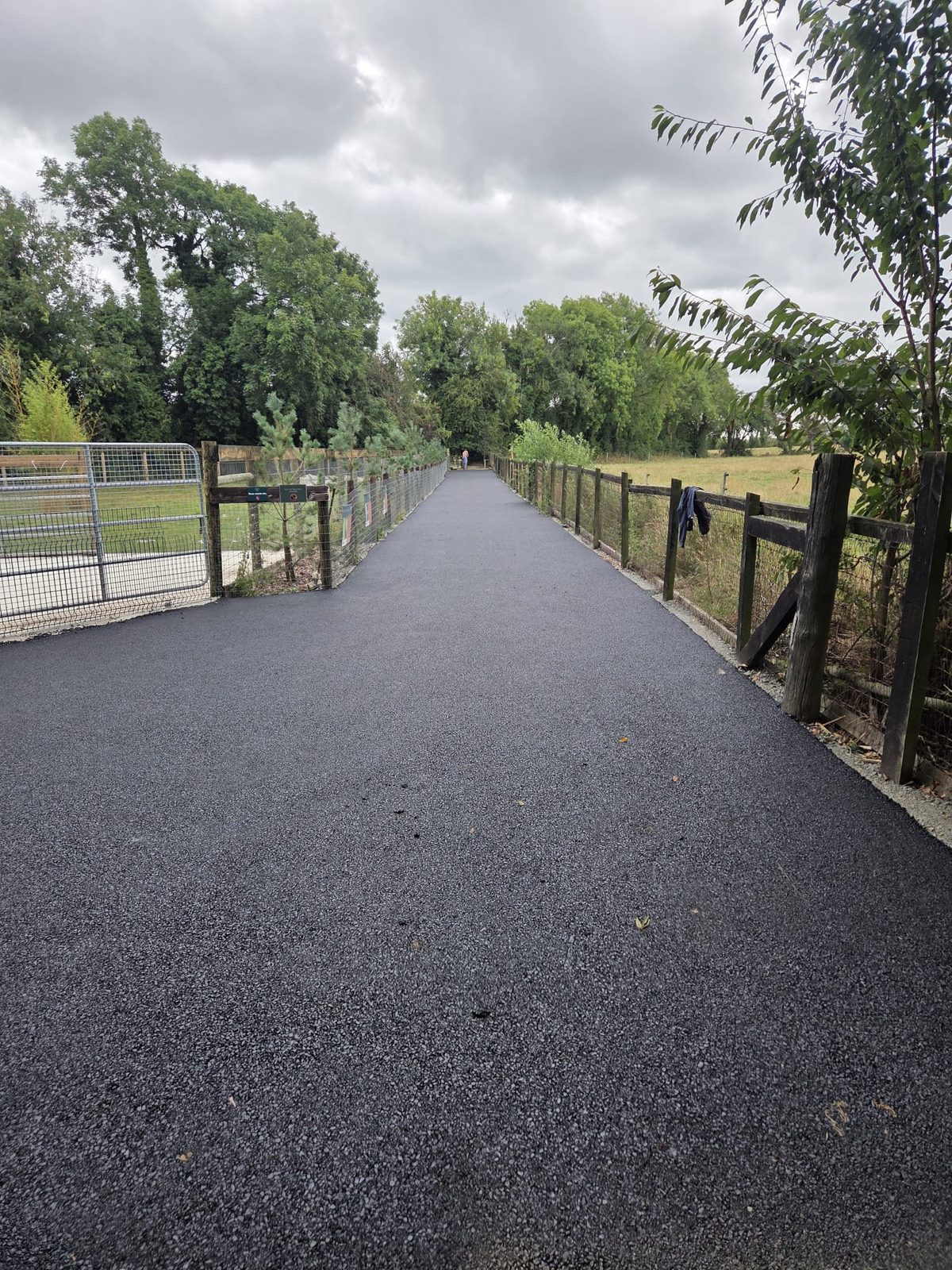 Long machine-laid tarmac lane running through parkland between post-and-rail fencing