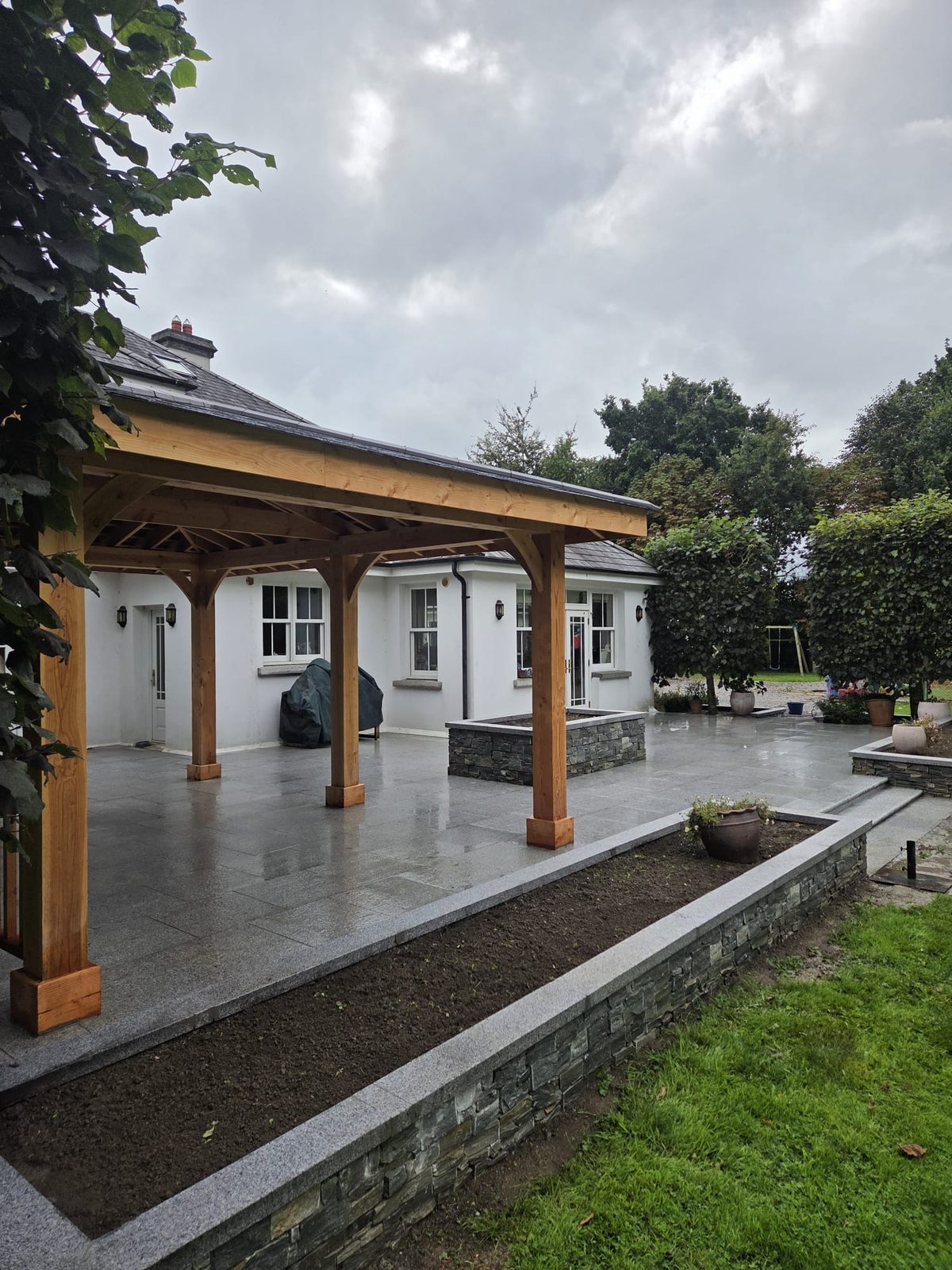Silver-grey granite patio with stone-clad raised beds and a cedar gazebo at a large country home, built by Delaney Tarmac