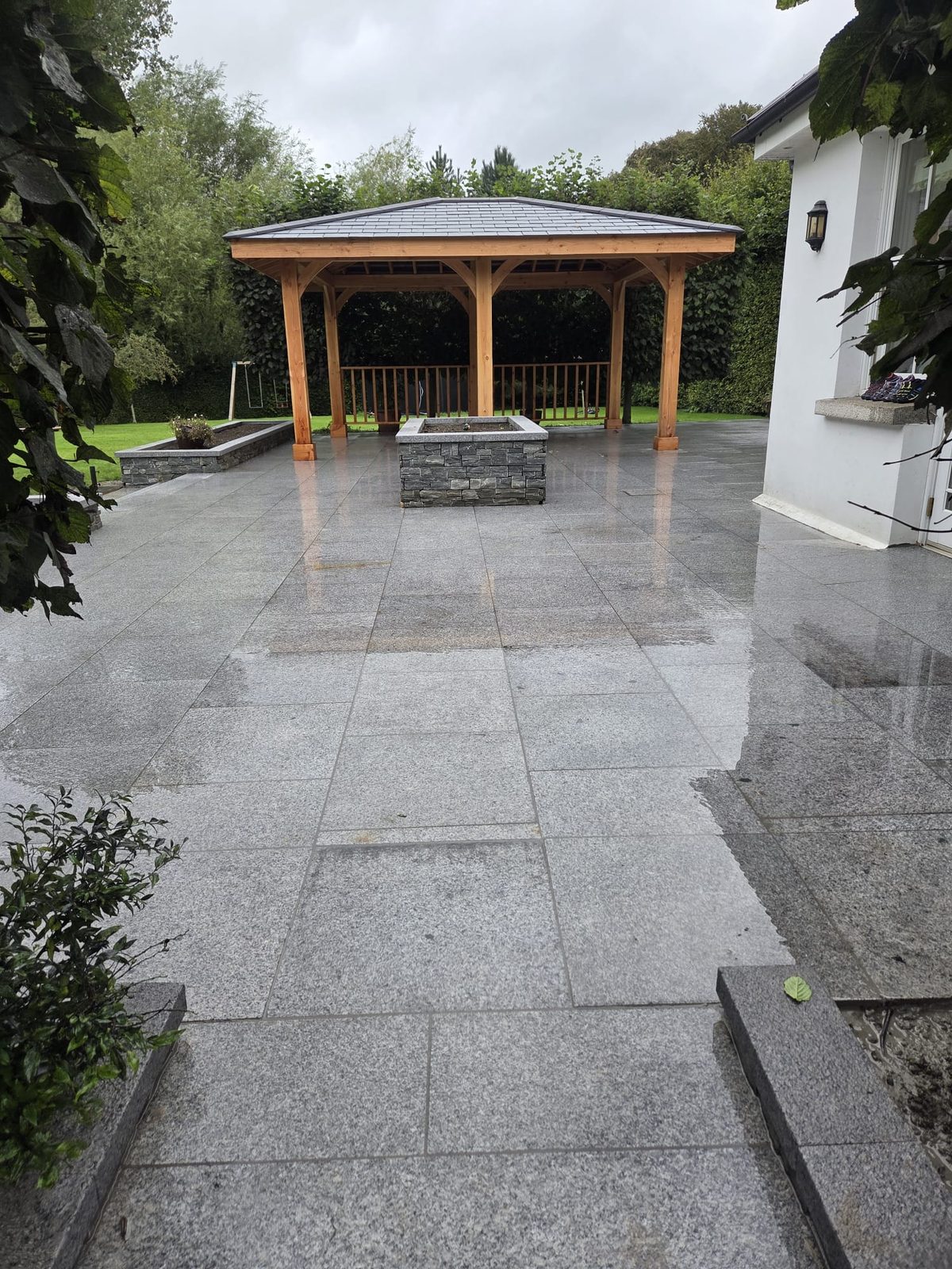 Granite patio with the cedar gazebo and a stone-clad raised bed at a large white country house