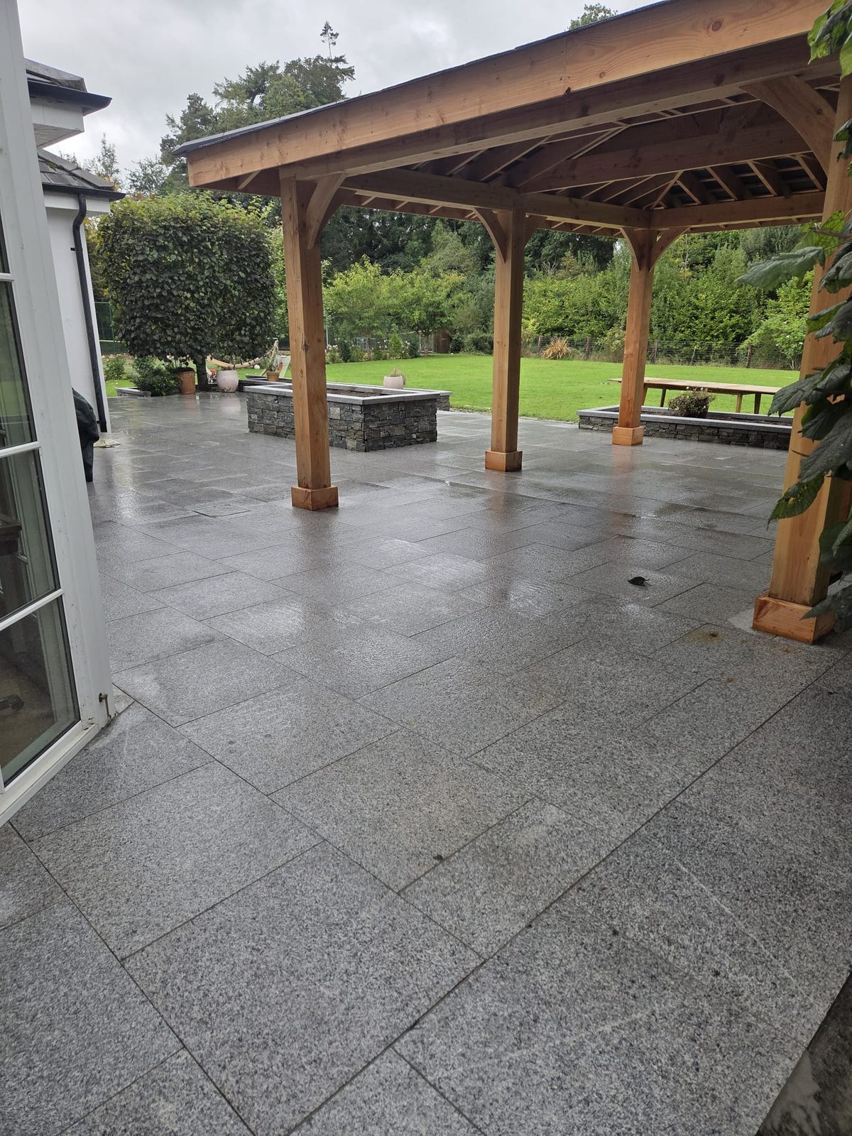 Silver-grey granite patio with a stone-clad raised bed and granite coping beside a country home