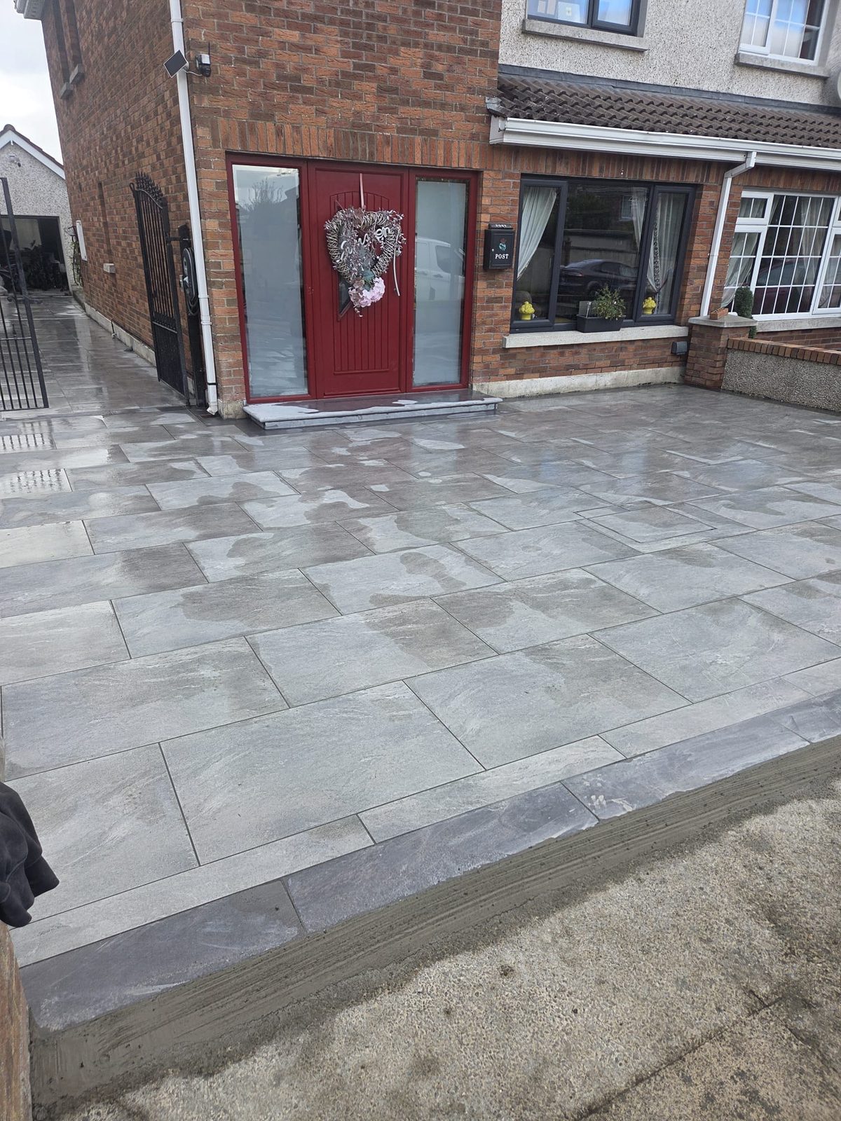 Grey porcelain forecourt with a granite step at the door of a red-door brick home, laid by Delaney Tarmac