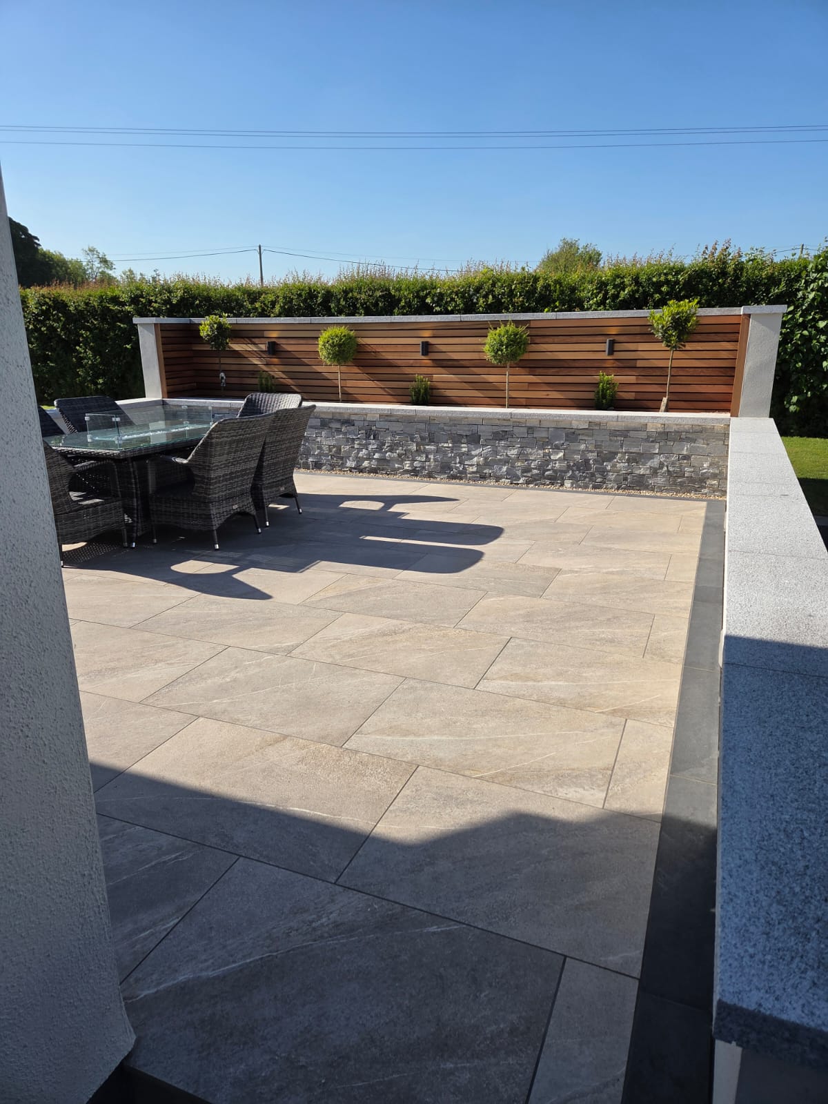 Premium grey porcelain patio with stone-clad raised wall, timber slat fencing and bay tree planters, a recent Delaney Tarmac install in south Dublin