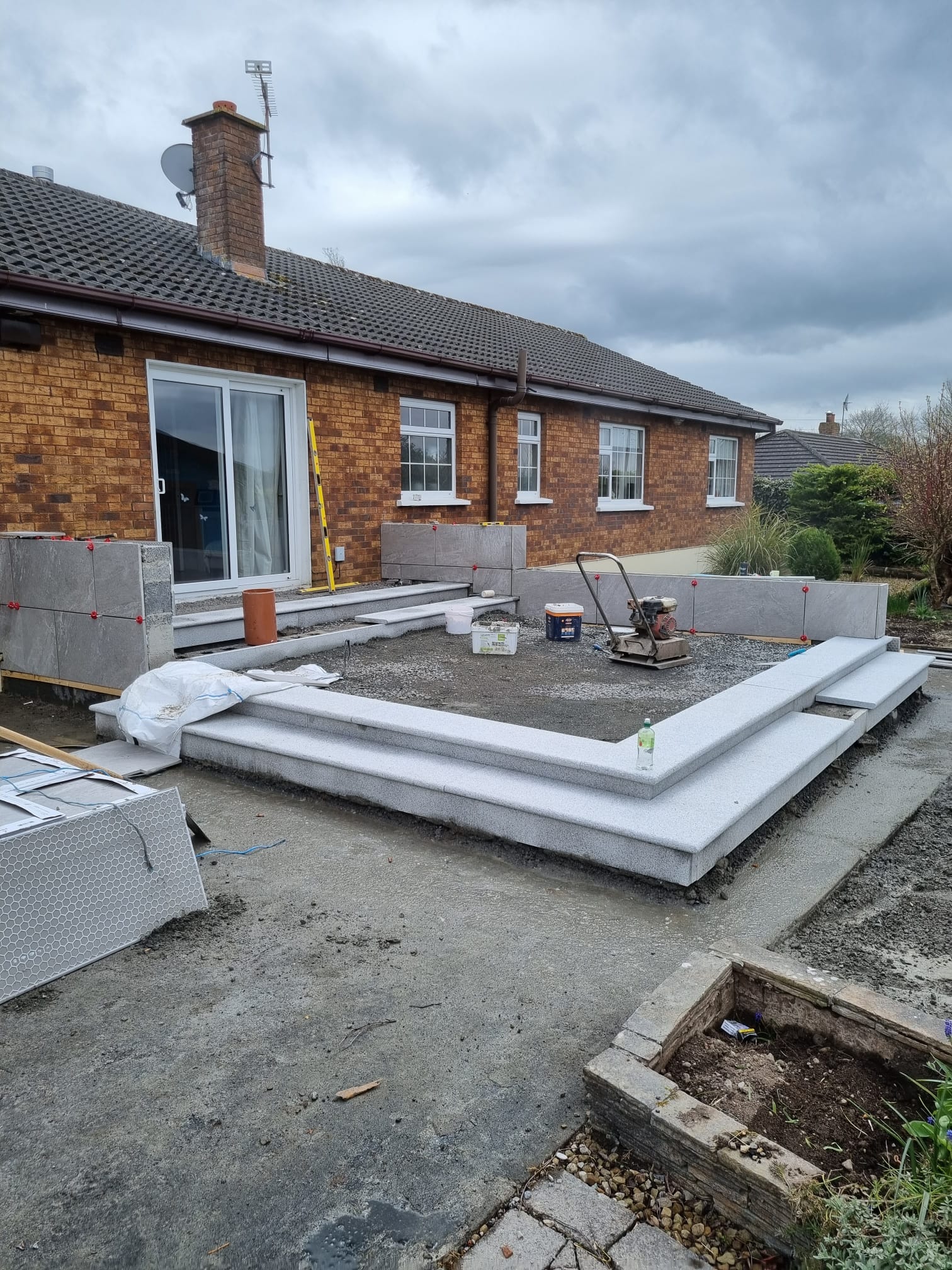 Raised porcelain patio part-built, showing the granite step surround and the compacted hardcore base before the porcelain was laid