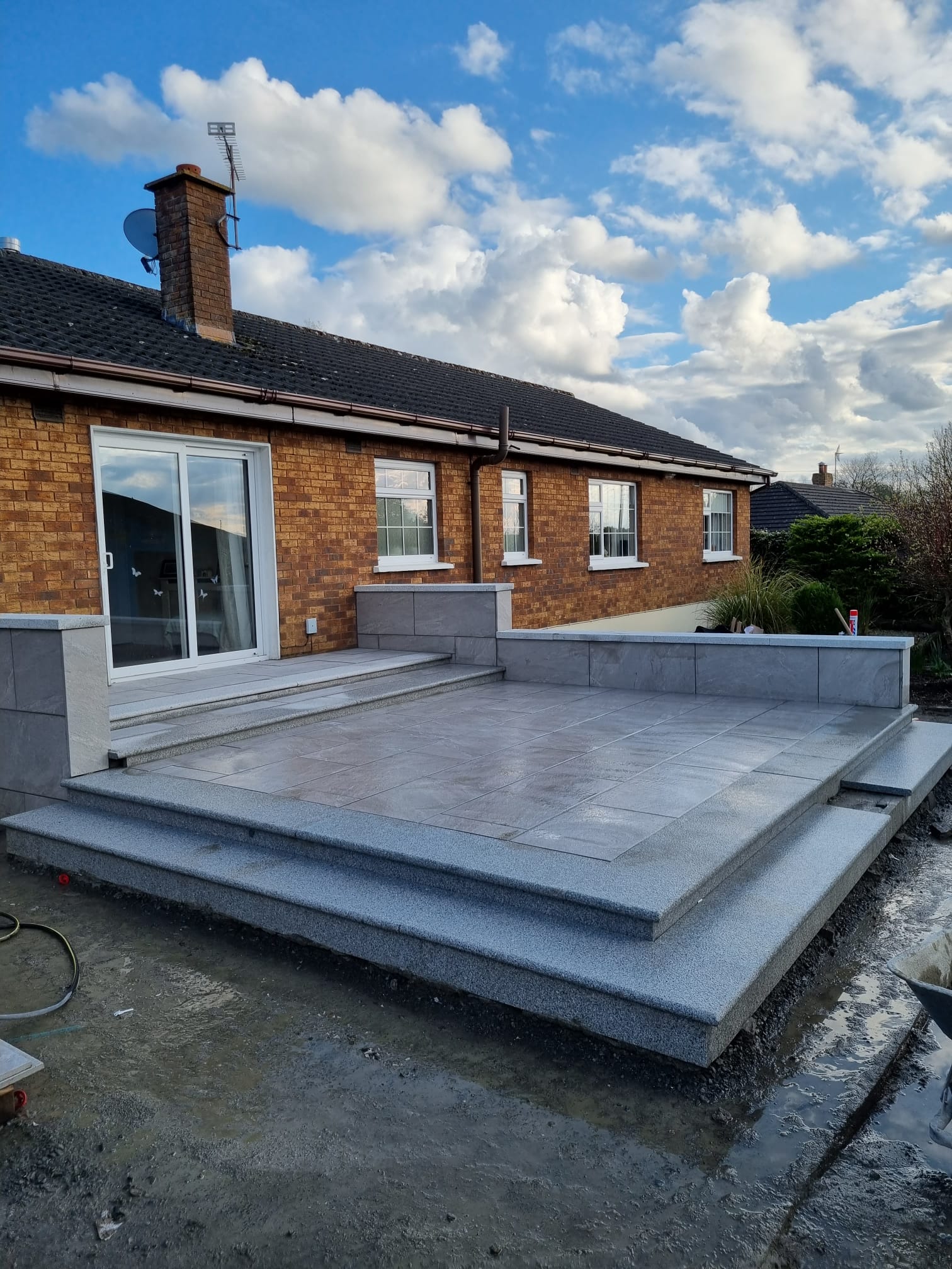 Raised grey porcelain patio with a granite step surround at a brick bungalow, laid by Delaney Tarmac