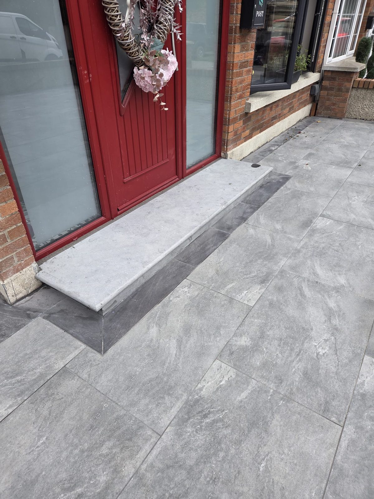 Granite step at the red front door set into a grey porcelain forecourt