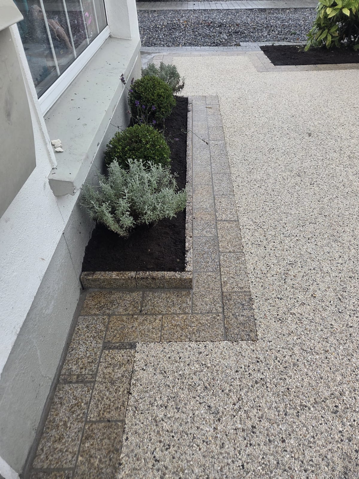 Planting bed behind a granite kerb, with the granite apron and the resin-bound drive