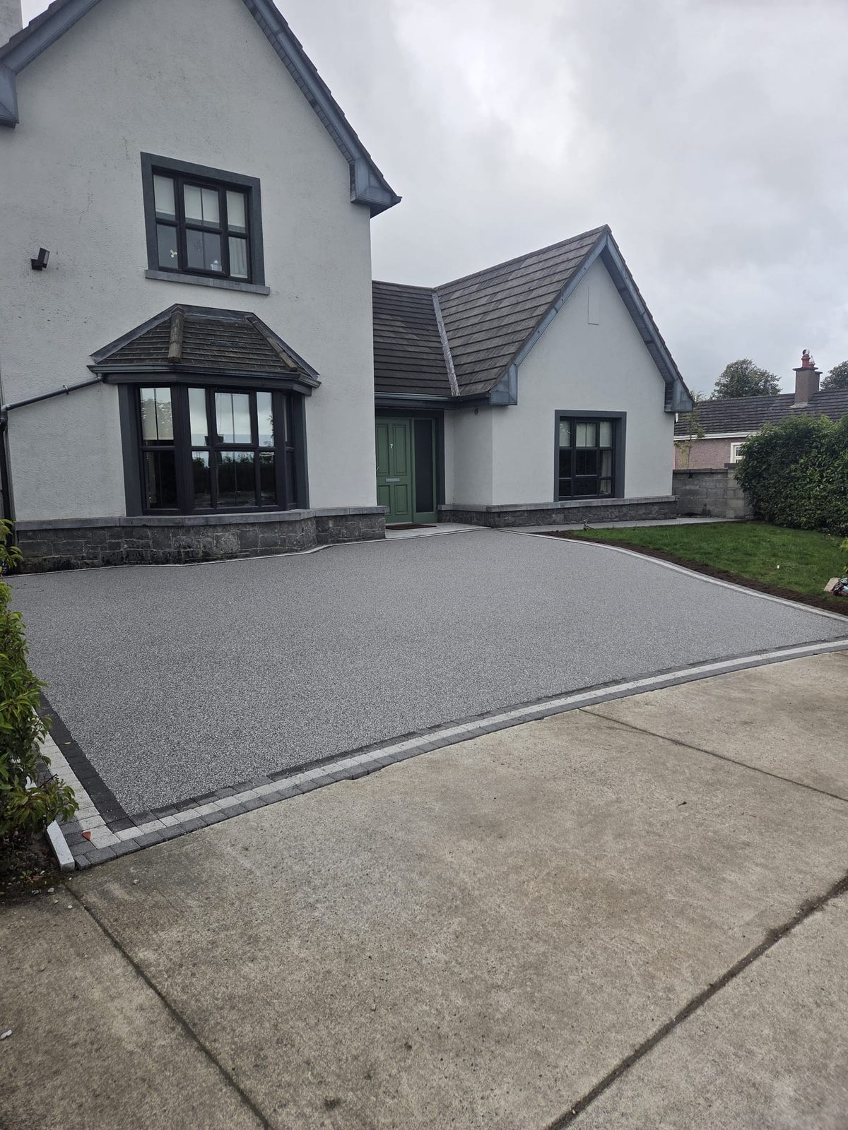 Silver resin bound driveway with a charcoal block border sweeping up to a green front door